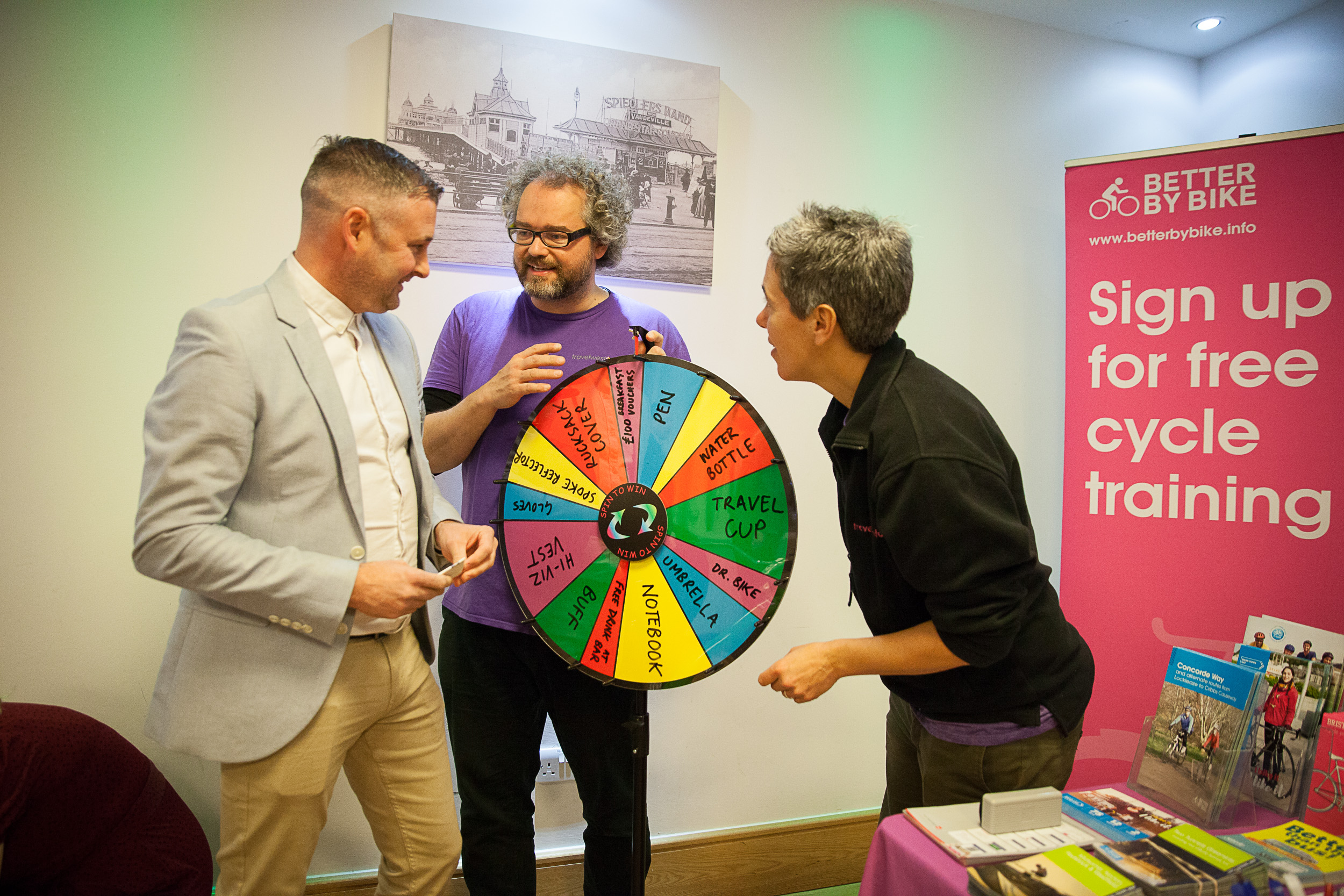 People talking and smiling at an engagement stall with a wheel of fortune game for sustainable prizes
