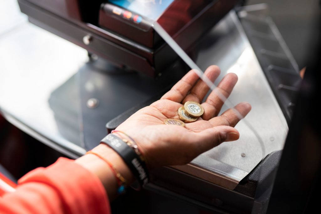 Hand holding three £1 coins next to a bus paying machine.