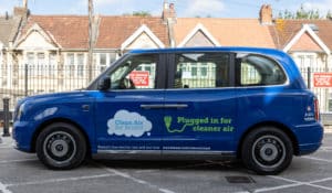 Blue electric taxi with the words Clean Air for Bristol. Plugged in for cleaner air. Bristol's free electric van and taxi trial.