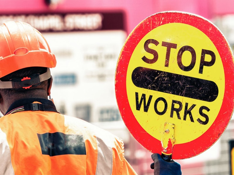 Image of a "Stop works" sign held by a traffic marshal in protective work gear.