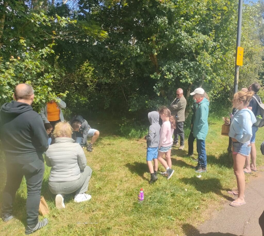 Photo of two participants kneeling to examine grasses, with a small group of people gathered around.
