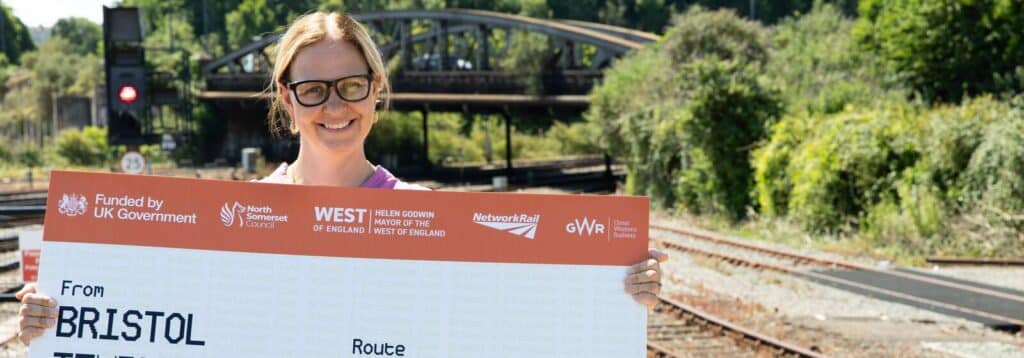 Mayor Helen Godwin in front of a rail track / bridge with an oversized rail ticket.