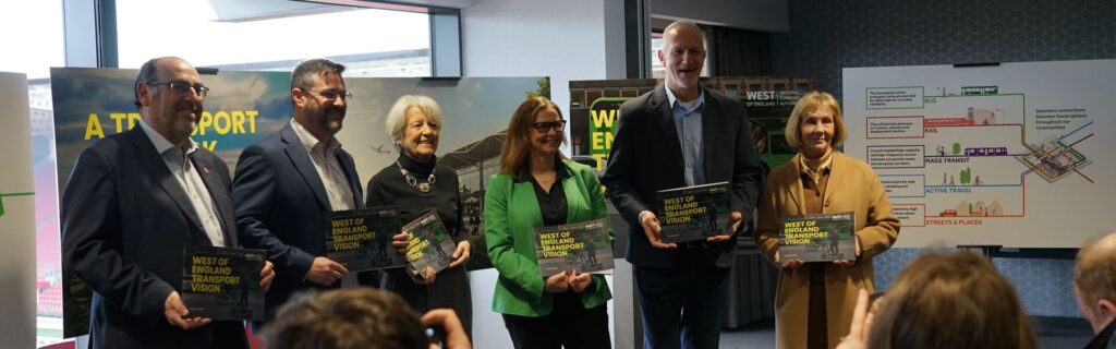 West of England UA leaders and the WoE Mayor standing in a line with the West of England Transport Vision information in the background.