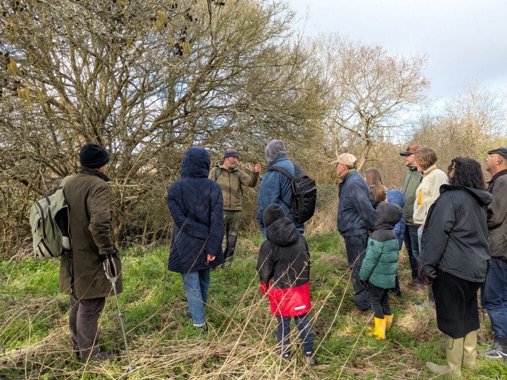 Photo of the walk leader discussing the poisonous Arum plant with a group of people gathered around.