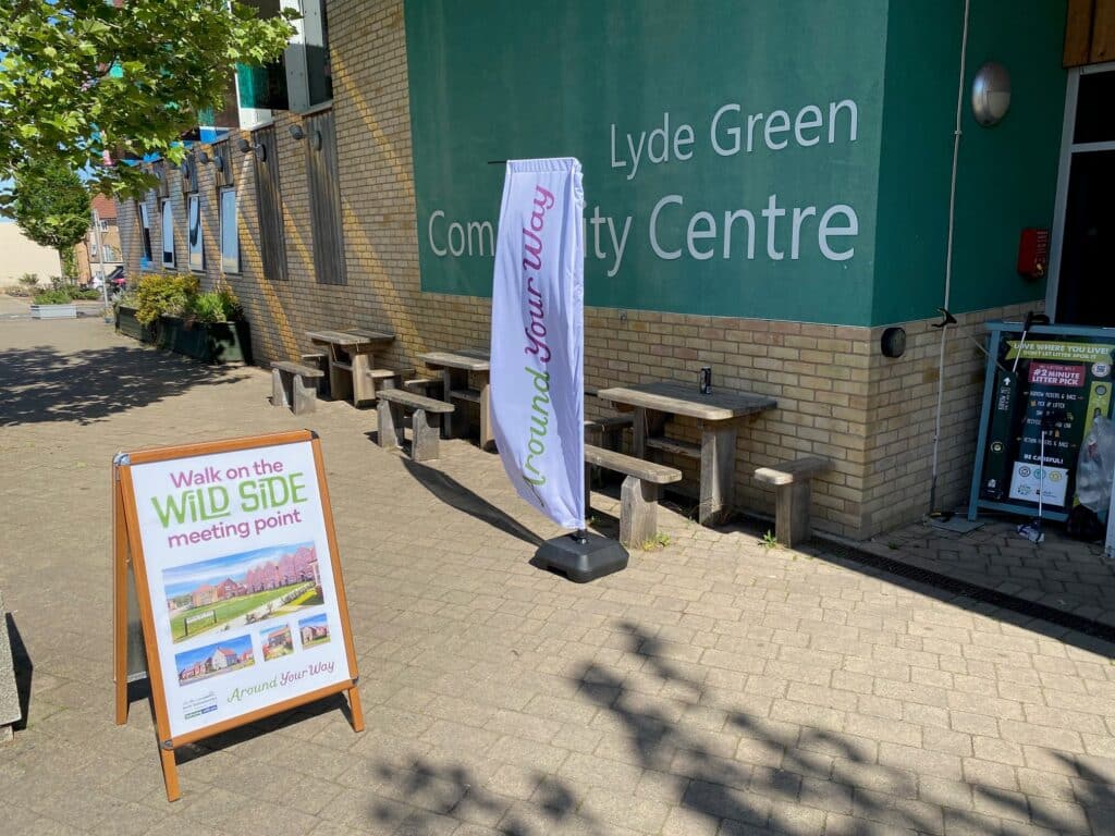 Photo of a promotional A-board sign and flag at the entrance to Lyde Green Community Centre marking the meeting point for the Walk on the Wild Side event.